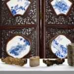 Background: A Chinese folding screen inset with underglaze blue porcelain plaques. Foreground: A collection of Chinese archaic jade carvings from a single owner collection.